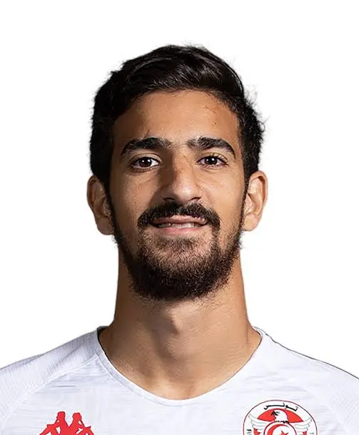 Portrait of a man with dark hair and beard, wearing a white sports jersey with red logos, against a white background.