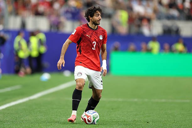 Soccer player in a red jersey number 3 dribbles a ball on a green field during a match.