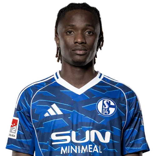 Portrait of a soccer player in a blue Schalke 04 jersey, facing the camera with sponsor logos visible on the front.
