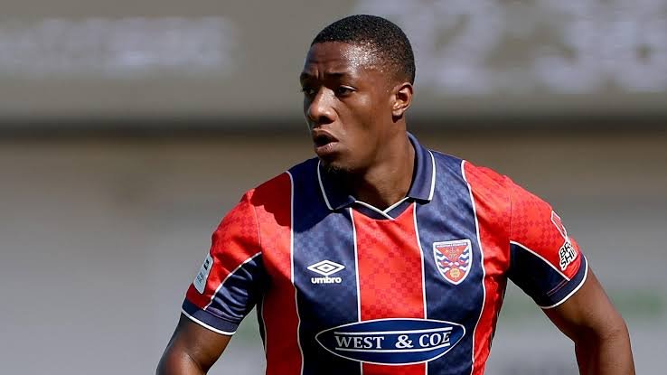 Soccer player in a red and blue striped jersey on the field, mid-game action.