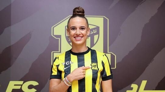 Portrait of a female soccer player wearing a yellow and black striped jersey with a crest, smiling at the camera. Portrait of a female soccer player wearing a yellow and black striped jersey with a crest, smiling at the camera.