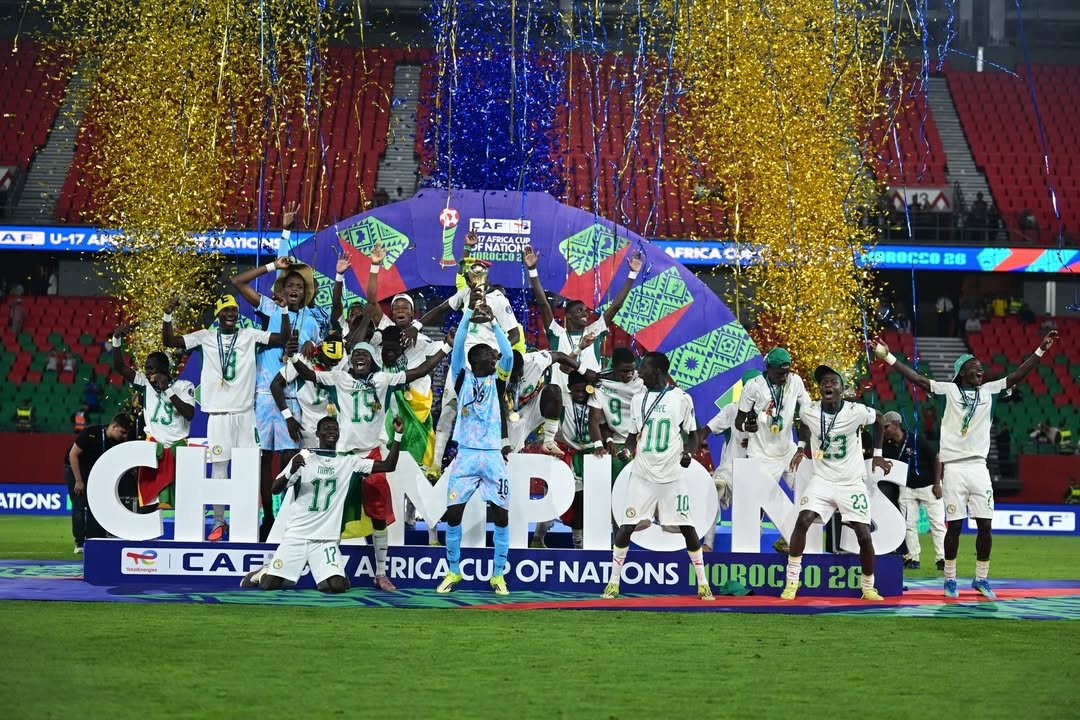 Soccer team in white uniforms celebrates a title with a trophy on a colorful stage and gold confetti falling around them. Soccer team in white uniforms celebrates a title with a trophy on a colorful stage and gold confetti falling around them.