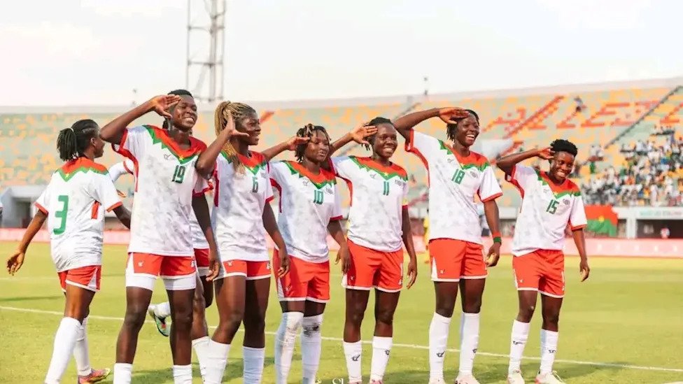 Women’s soccer team standing in a line on the field, saluting during the national anthem or pre-match ritual. Women’s soccer team standing in a line on the field, saluting during the national anthem or pre-match ritual.