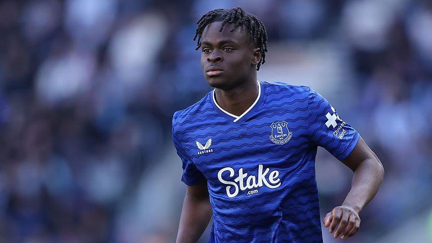 Soccer player in a blue Everton jersey running on the field during a match with Stake sponsor visible on the chest edge of the shirt.