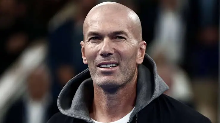 Close-up of a smiling bald man wearing a gray-hooded jacket, facing the camera.