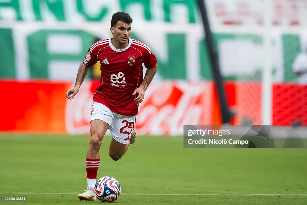 Soccer player in a red jersey dribbling the ball on a green field during a match with advertising boards in the background. Soccer player in a red jersey dribbling the ball on a green field during a match with advertising boards in the background.