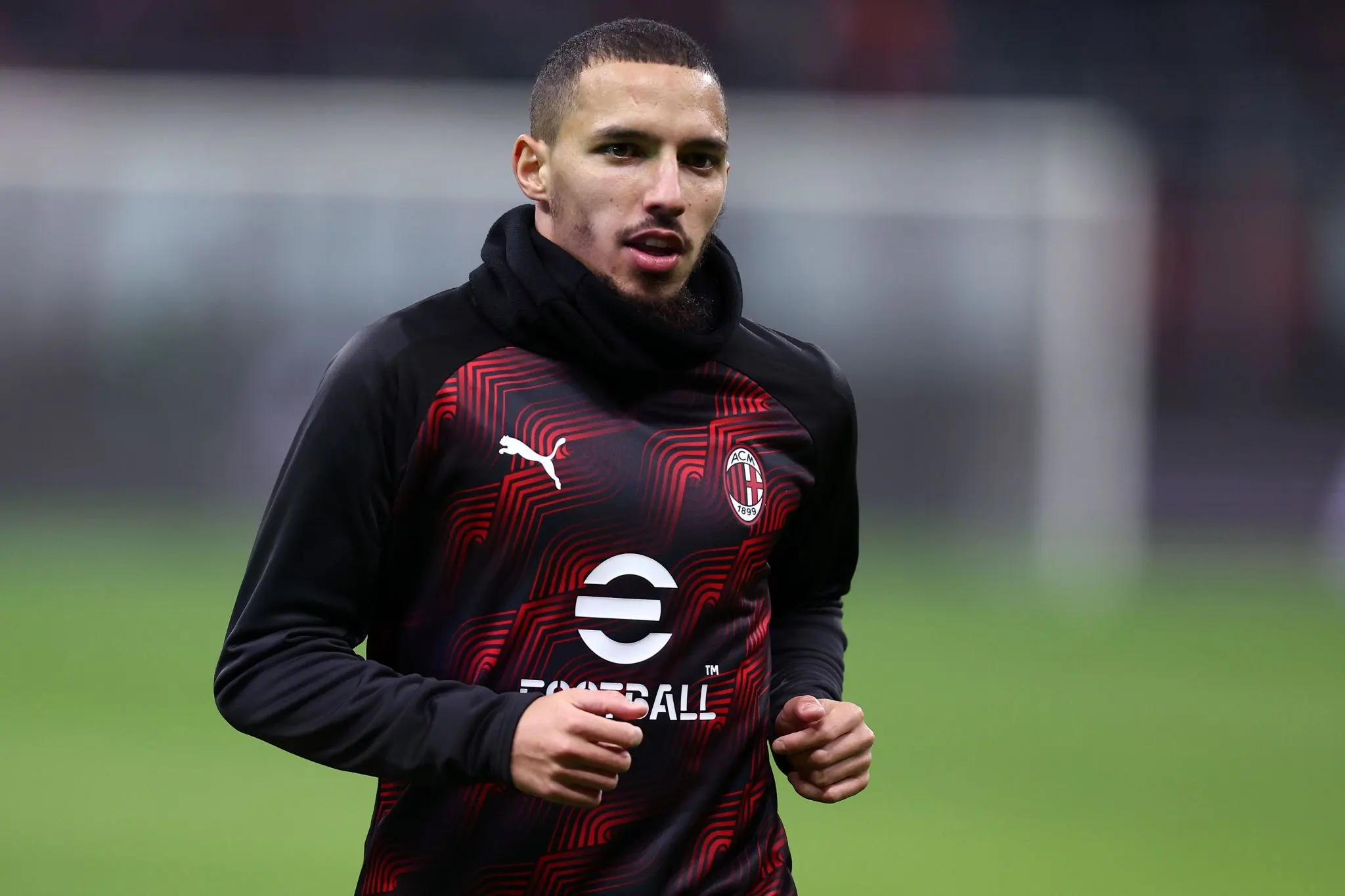 Soccer player wearing an AC Milan training jersey runs on a grass field during practice, focus on upper body and face. Soccer player wearing an AC Milan training jersey runs on a grass field during practice, focus on upper body and face.