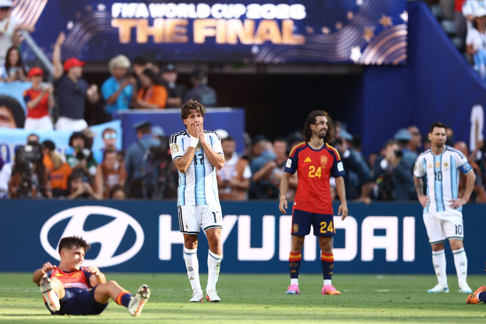 Argentine player in light-blue stripes covers his mouth with his hands during the final, with fans and players in the background.