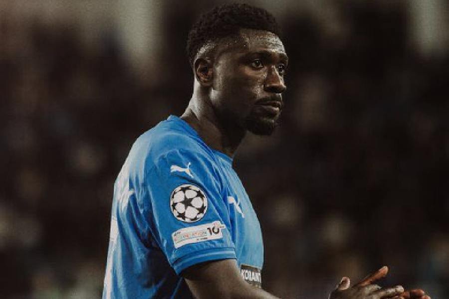 Male soccer player in a blue jersey on the field, turned toward the right, with a Champions League patch on the sleeve.