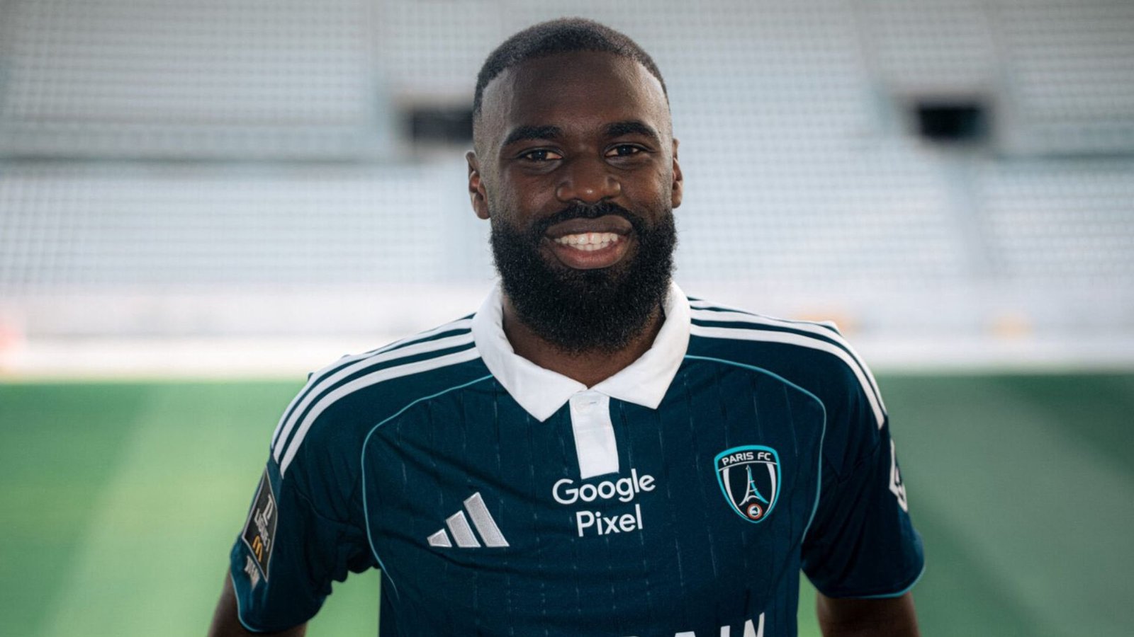 Smiling Black soccer player in a Paris FC jersey on a green field. Smiling Black soccer player in a Paris FC jersey on a green field.