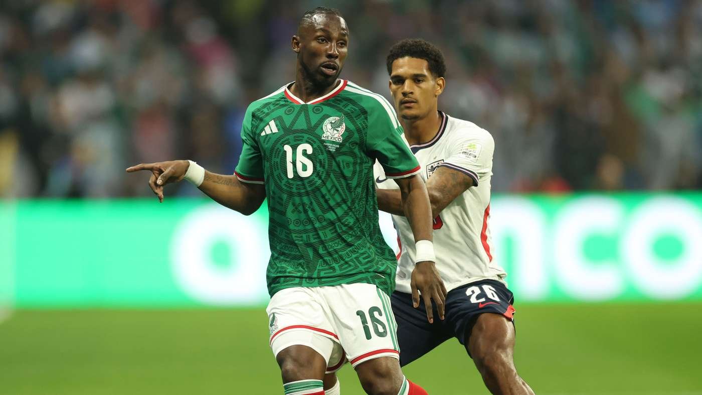 Soccer player in green Mexico jersey #16 points as he challenges an opponent during a match.