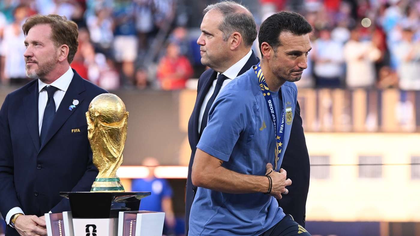 Athlete in a blue shirt with a medal walks past a large World Cup trophy as officials stand nearby. Athlete in a blue shirt with a medal walks past a large World Cup trophy as officials stand nearby.