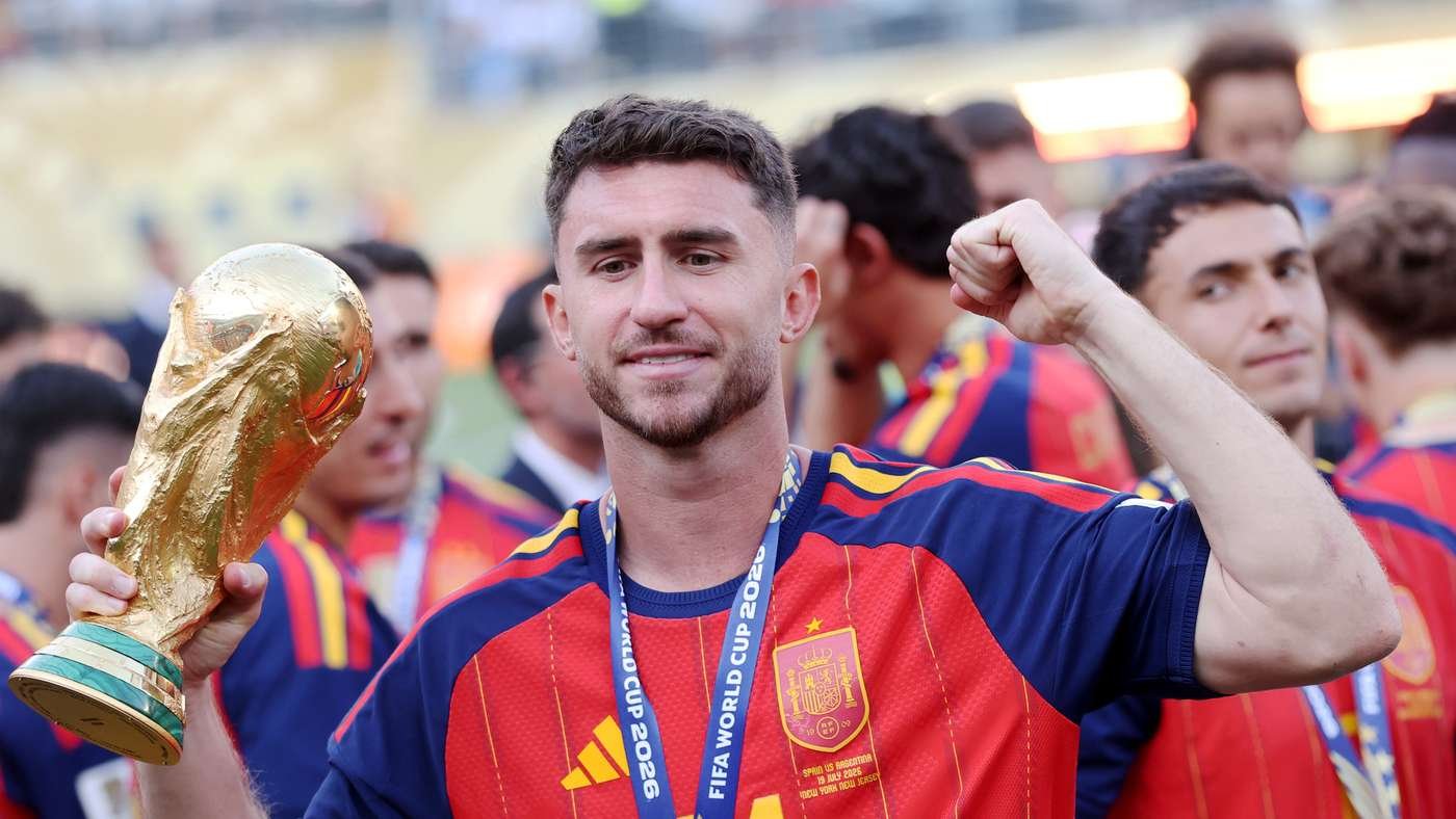 Soccer player in red-blue jersey lifting a golden trophy in celebration, teammates in the background. Soccer player in red-blue jersey lifting a golden trophy in celebration, teammates in the background.