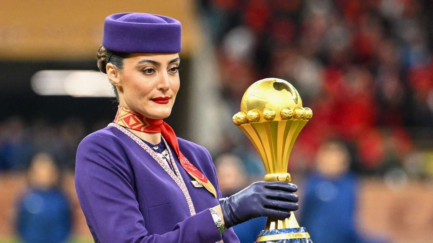 Woman in a purple uniform and hat holds a tall gold trophy at a stadium ceremony. Woman in a purple uniform and hat holds a tall gold trophy at a stadium ceremony.