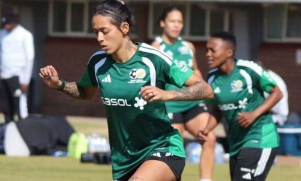 Female soccer players in green training kits sprint on a grassy field during practice, with the SASOL logo visible on their shirts.