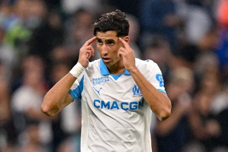 Soccer player in a white Marseille jersey with CMA CGM sponsor touching his temples with both hands, signaling focus or concentration on the field