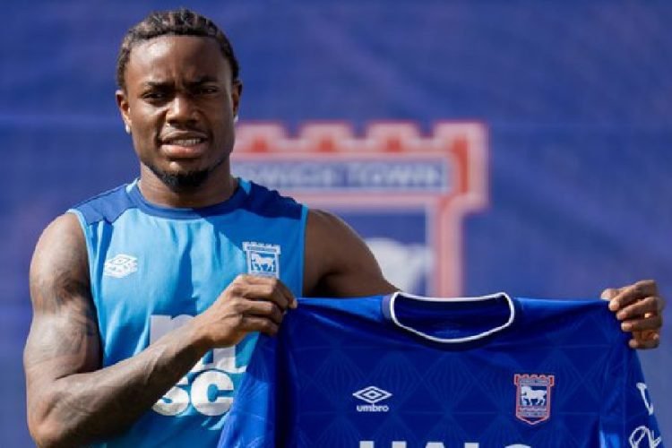 Male footballer in a blue training kit holds up a blue club jersey against a blue background. Male footballer in a blue training kit holds up a blue club jersey against a blue background.