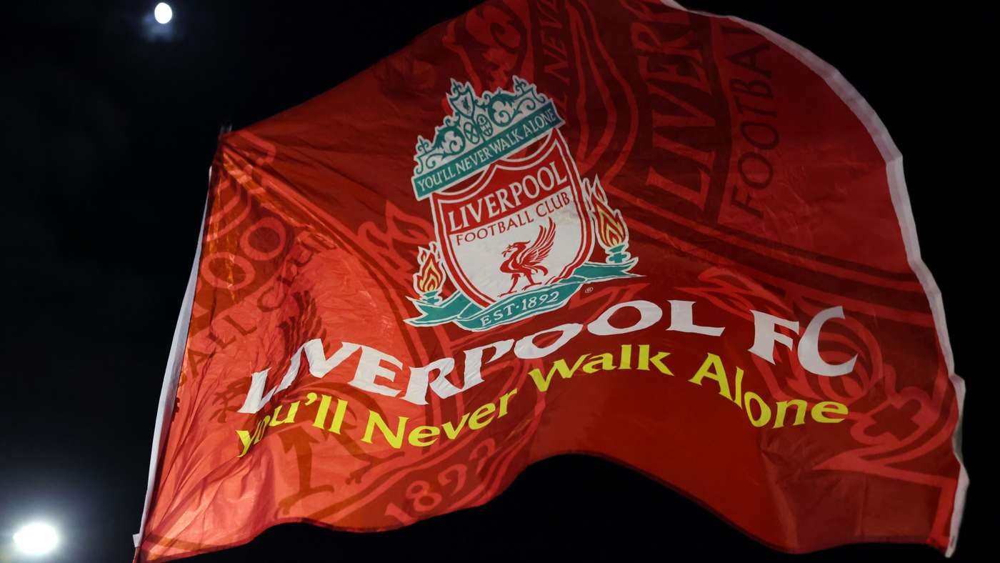 Red Liverpool FC flag waving at night with crest and slogan 'You'll Never Walk Alone' visible. Red Liverpool FC flag waving at night with crest and slogan 'You'll Never Walk Alone' visible.