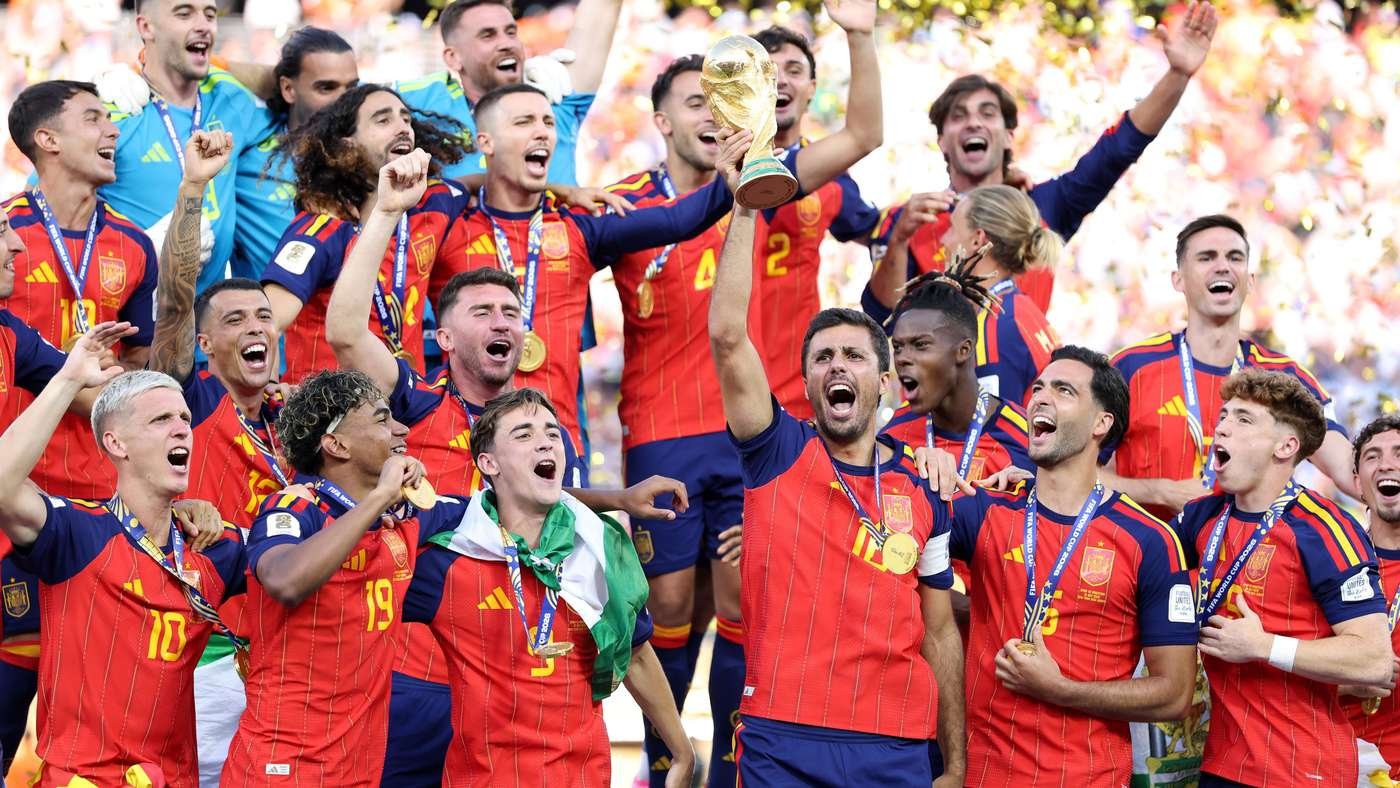 Spain national football team celebrating their win, lifting the trophy amid teammates with gold medals as confetti falls from a cheering crowd.