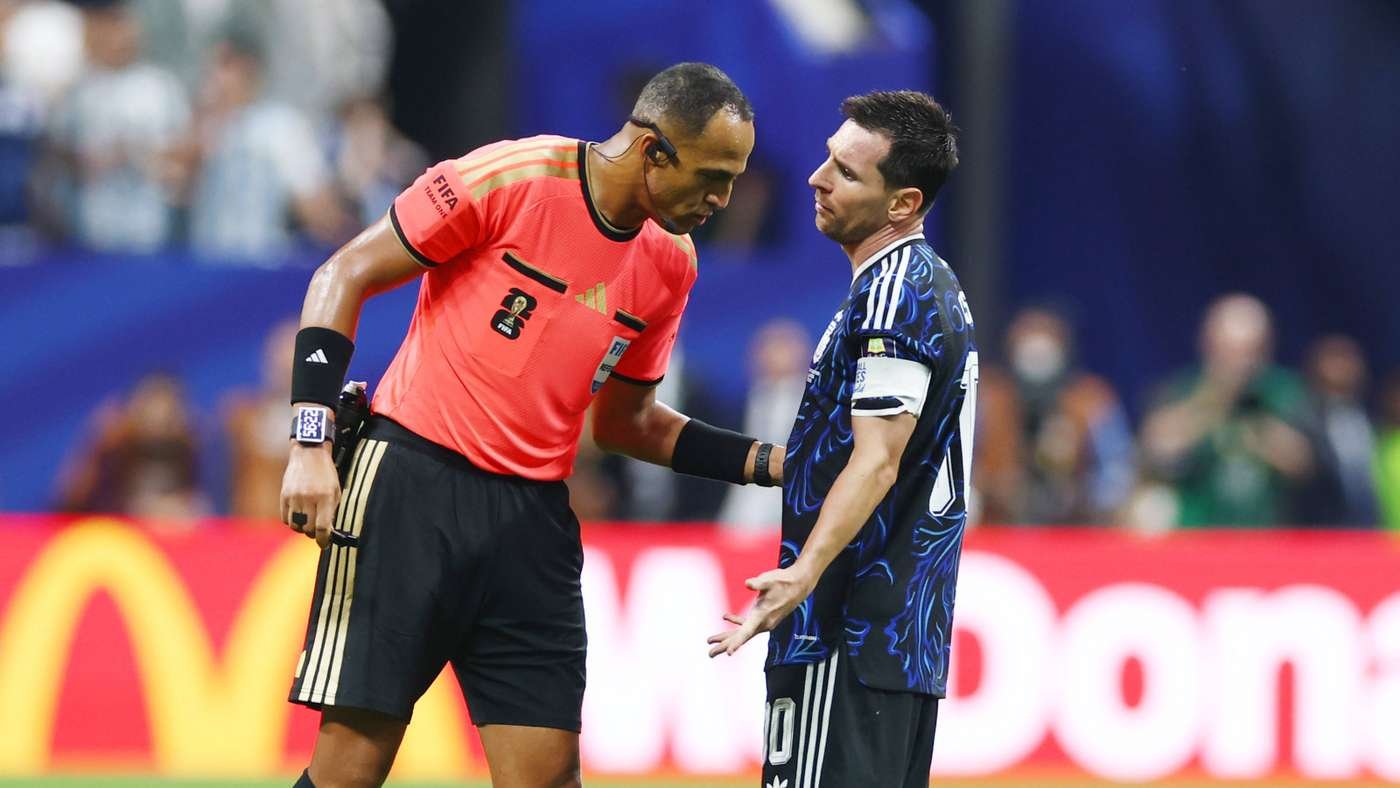 Soccer referee in a pink shirt confronts a player in a blue jersey during a heated discussion on the field. Soccer referee in a pink shirt confronts a player in a blue jersey during a heated discussion on the field.