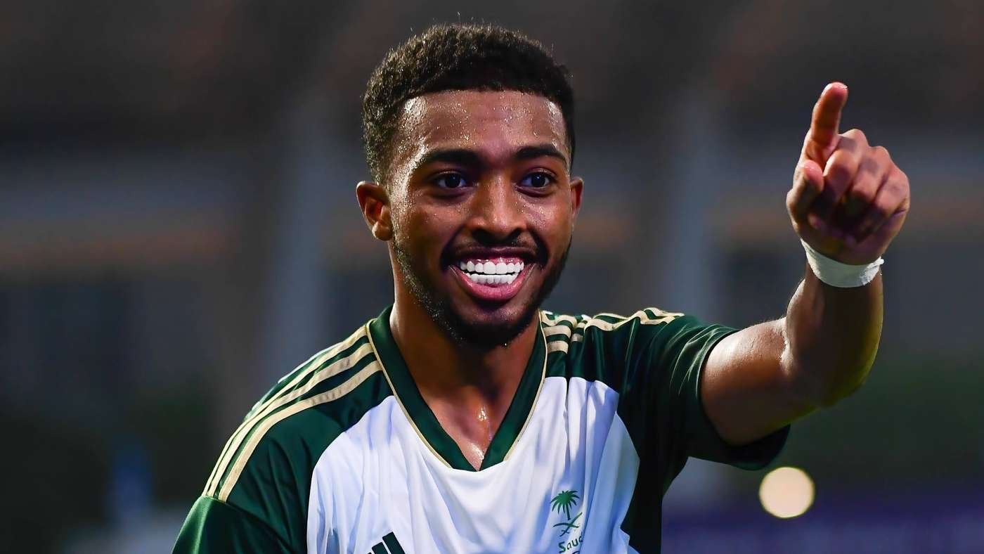 Athlete in a green and white jersey smiles and points forward in celebration.