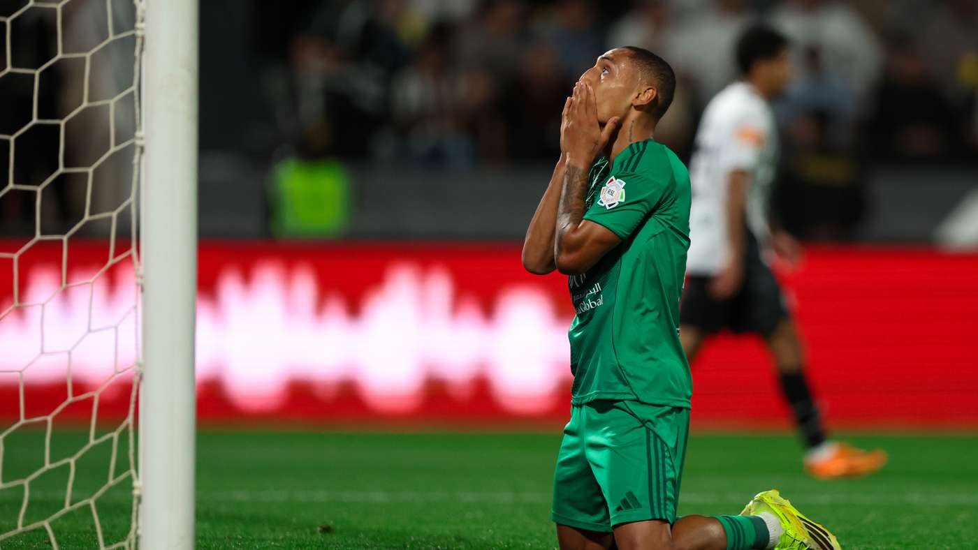 Soccer player in a green kit kneels by the goal, hands covering his face in disappointment. Soccer player in a green kit kneels by the goal, hands covering his face in disappointment.
