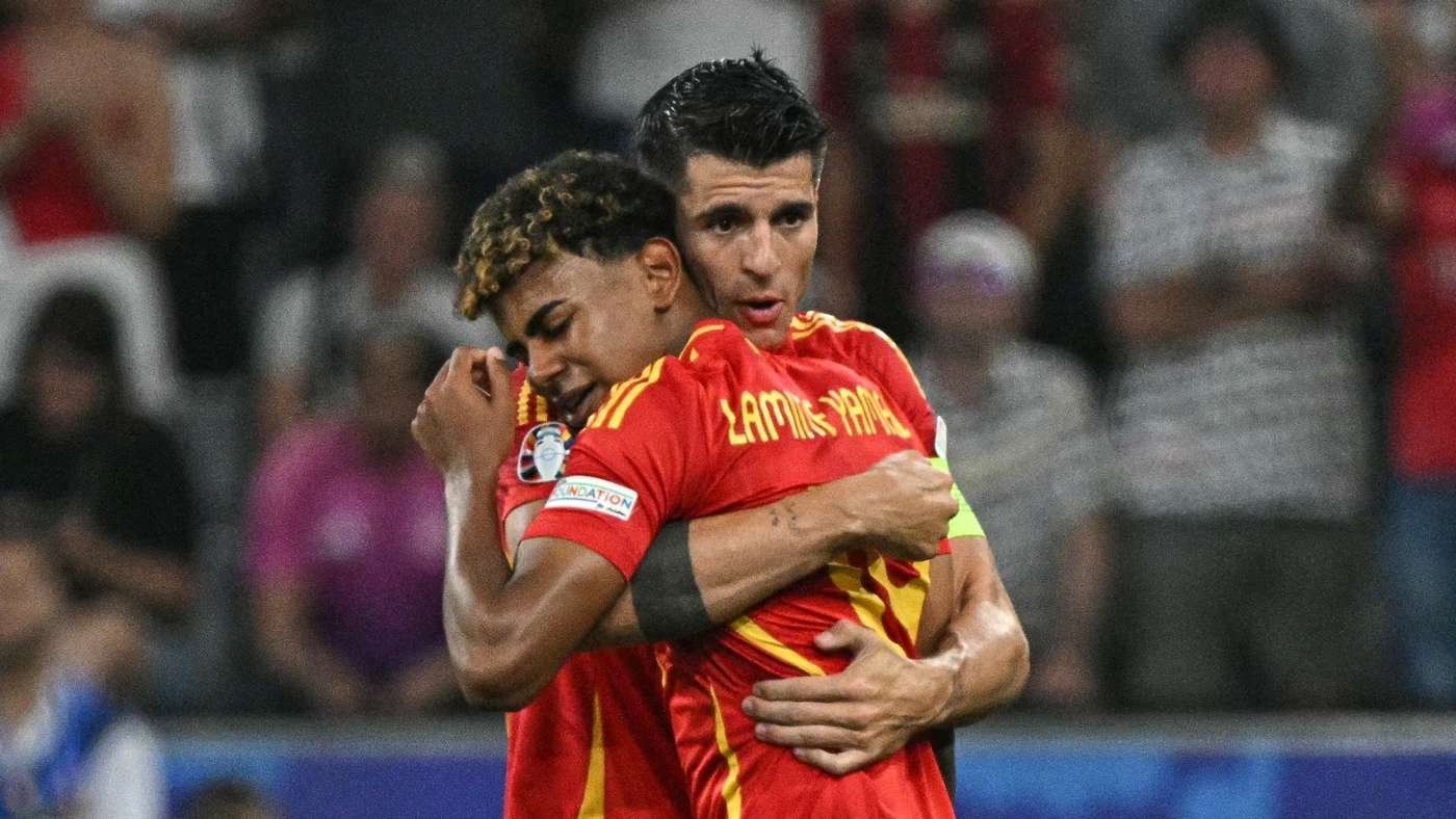Two soccer players in red and yellow jerseys embrace in celebration on the pitch. Two soccer players in red and yellow jerseys embrace in celebration on the pitch.