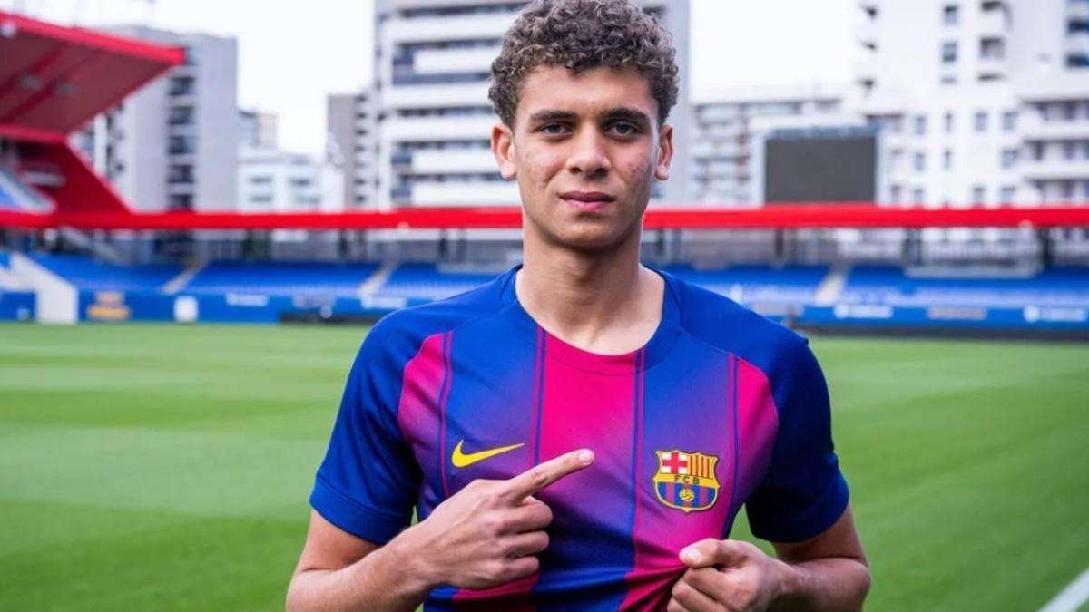 Young man in a FC Barcelona jersey on a grass soccer field, pointing to the team crest on his chest. Young man in a FC Barcelona jersey on a grass soccer field, pointing to the team crest on his chest.
