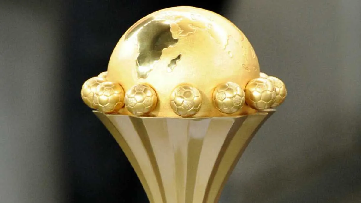 Gold trophy with a spherical world on top and small soccer balls lining the rim, set against a dark background.