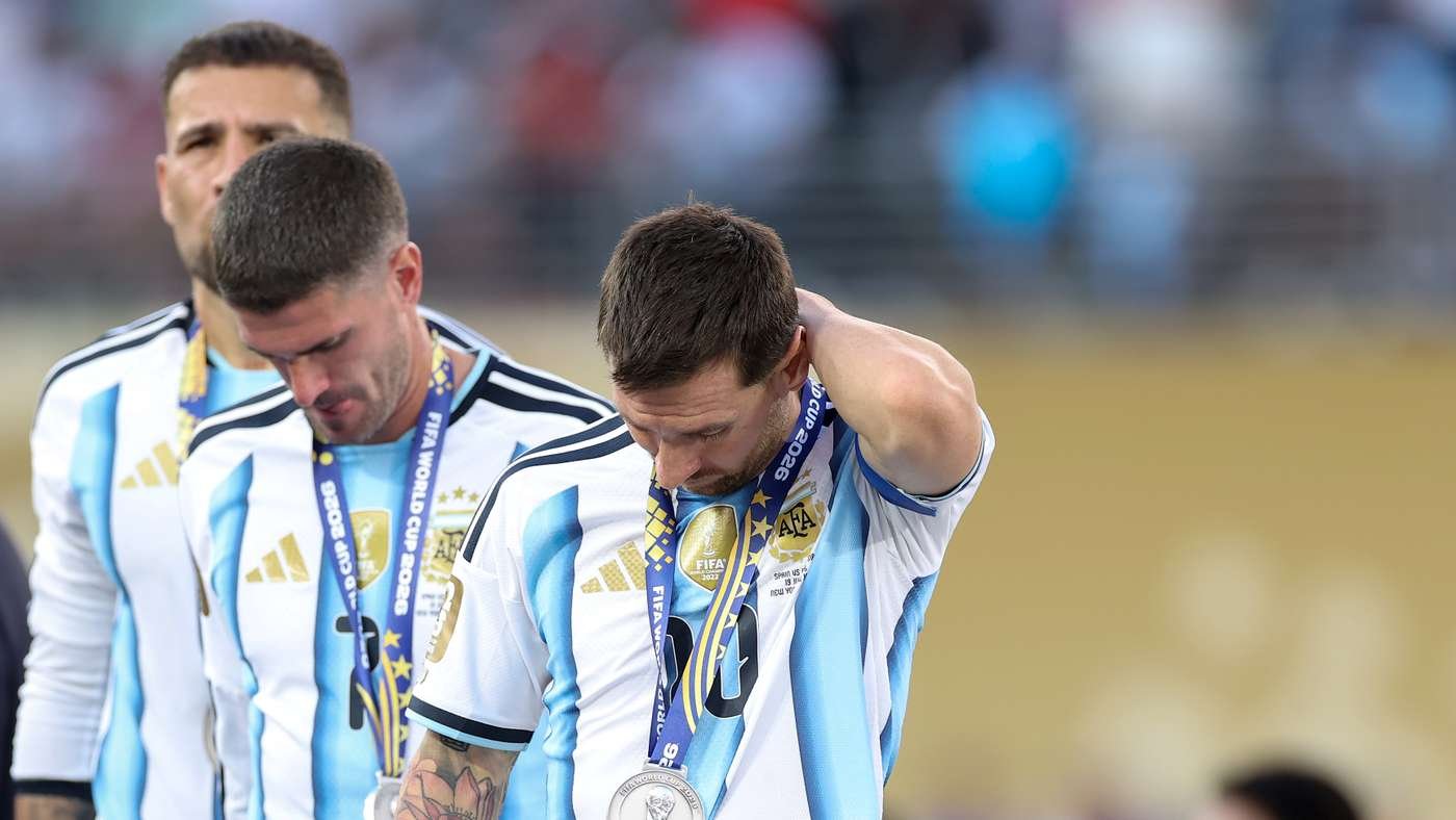 Two Argentine soccer players in white-and-blue striped jerseys wear gold medals around their necks after a match, one touching his neck.
