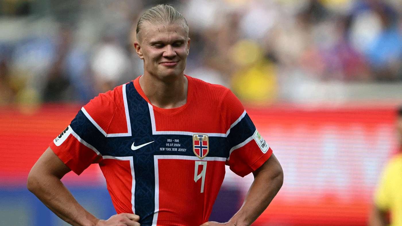 Soccer player wearing a red jersey with a blue Nordic cross, hands on hips on the pitch with a blurred stadium behind him Soccer player wearing a red jersey with a blue Nordic cross, hands on hips on the pitch with a blurred stadium behind him