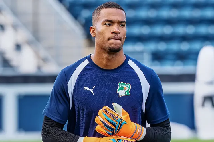 Soccer goalkeeper in a blue jersey with orange gloves, standing on a field with empty stadium seats behind. Soccer goalkeeper in a blue jersey with orange gloves, standing on a field with empty stadium seats behind.