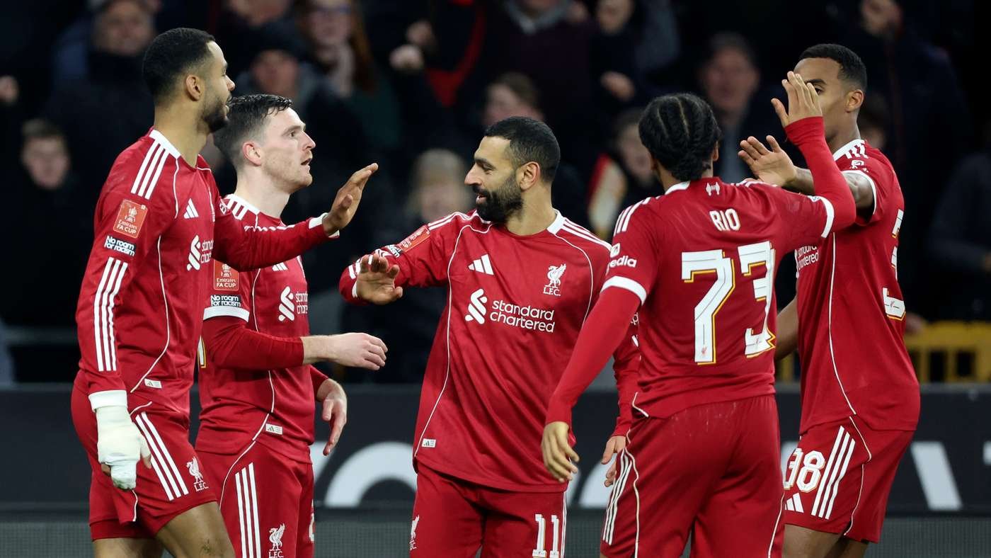 Liverpool players in red celebrate a goal on the pitch, high-fiving and greeting each other amid a crowd. Liverpool players in red celebrate a goal on the pitch, high-fiving and greeting each other amid a crowd.