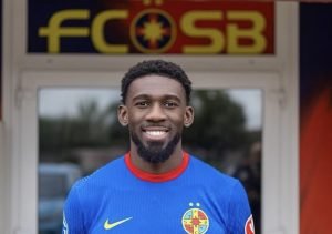 Portrait of a smiling male football player in a blue jersey standing in front of a building with an FCOSB sign above the door.