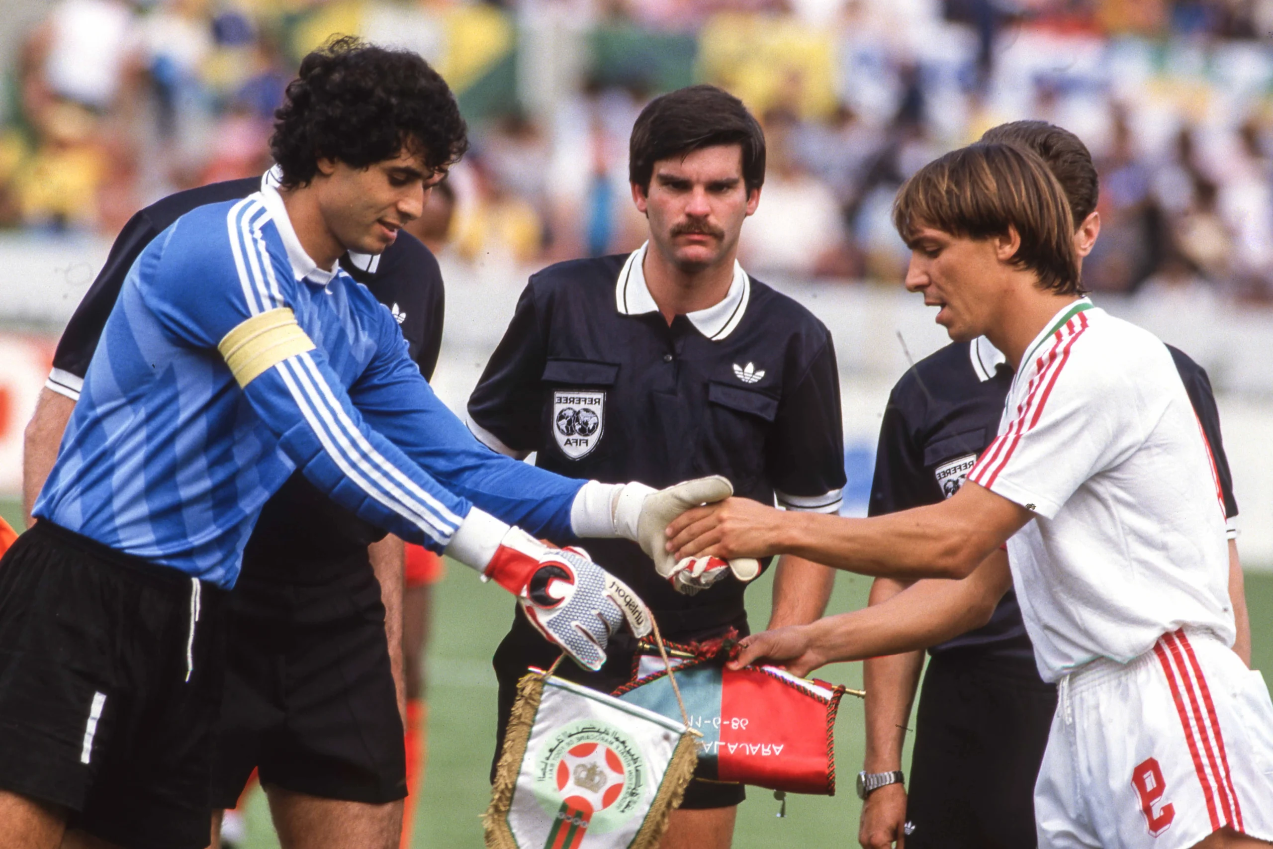 Two soccer players shake hands before a match as a referee looks on in the center. Two soccer players shake hands before a match as a referee looks on in the center.