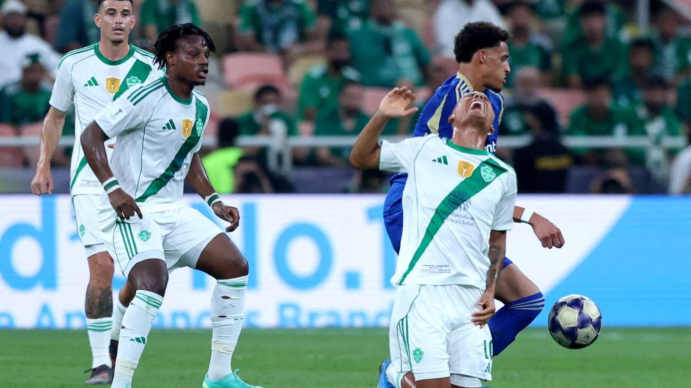 Soccer players in white and green kits compete for the ball on the field; foreground player appears to celebrate or shout while others watch. Soccer players in white and green kits compete for the ball on the field; foreground player appears to celebrate or shout while others watch.