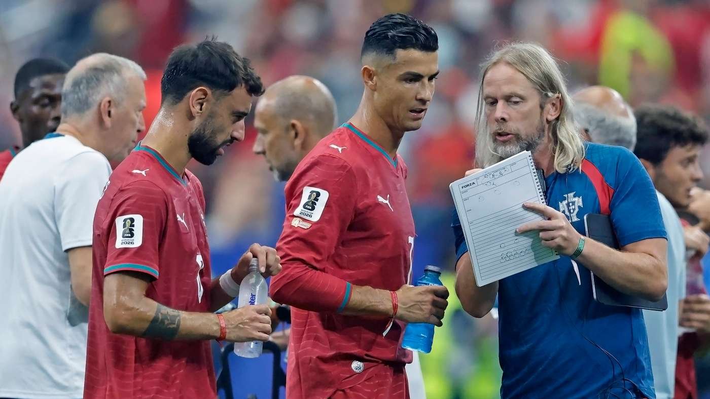 Portugal soccer players in red jerseys conference with a coach holding a clipboard on the sideline. Portugal soccer players in red jerseys conference with a coach holding a clipboard on the sideline.