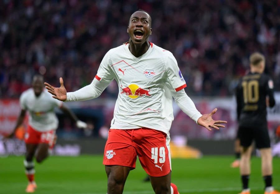 Soccer player in a white RB Leipzig jersey and red shorts celebrating with arms outstretched on the pitch, crowd in the background. Soccer player in a white RB Leipzig jersey and red shorts celebrating with arms outstretched on the pitch, crowd in the background.