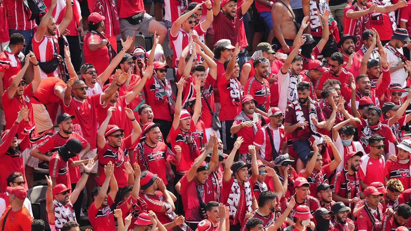 Large crowd of fans wearing red cheering with arms raised at a stadium. Large crowd of fans wearing red cheering with arms raised at a stadium.