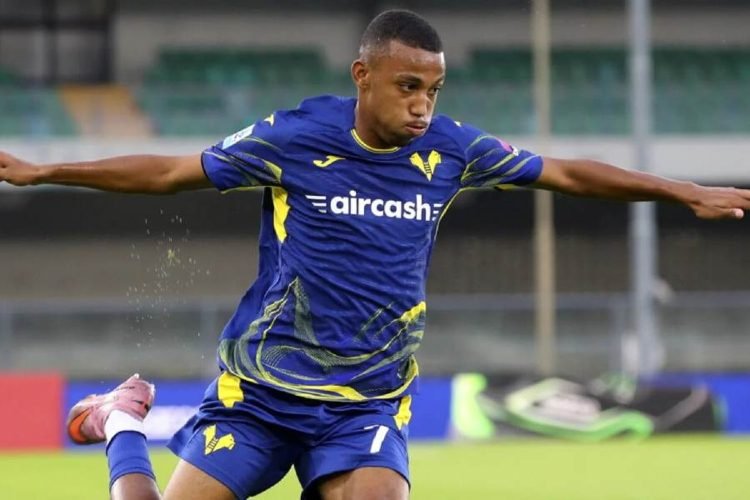 Soccer player in blue and yellow kit extends arms while kicking the ball on a grass field. Soccer player in blue and yellow kit extends arms while kicking the ball on a grass field.