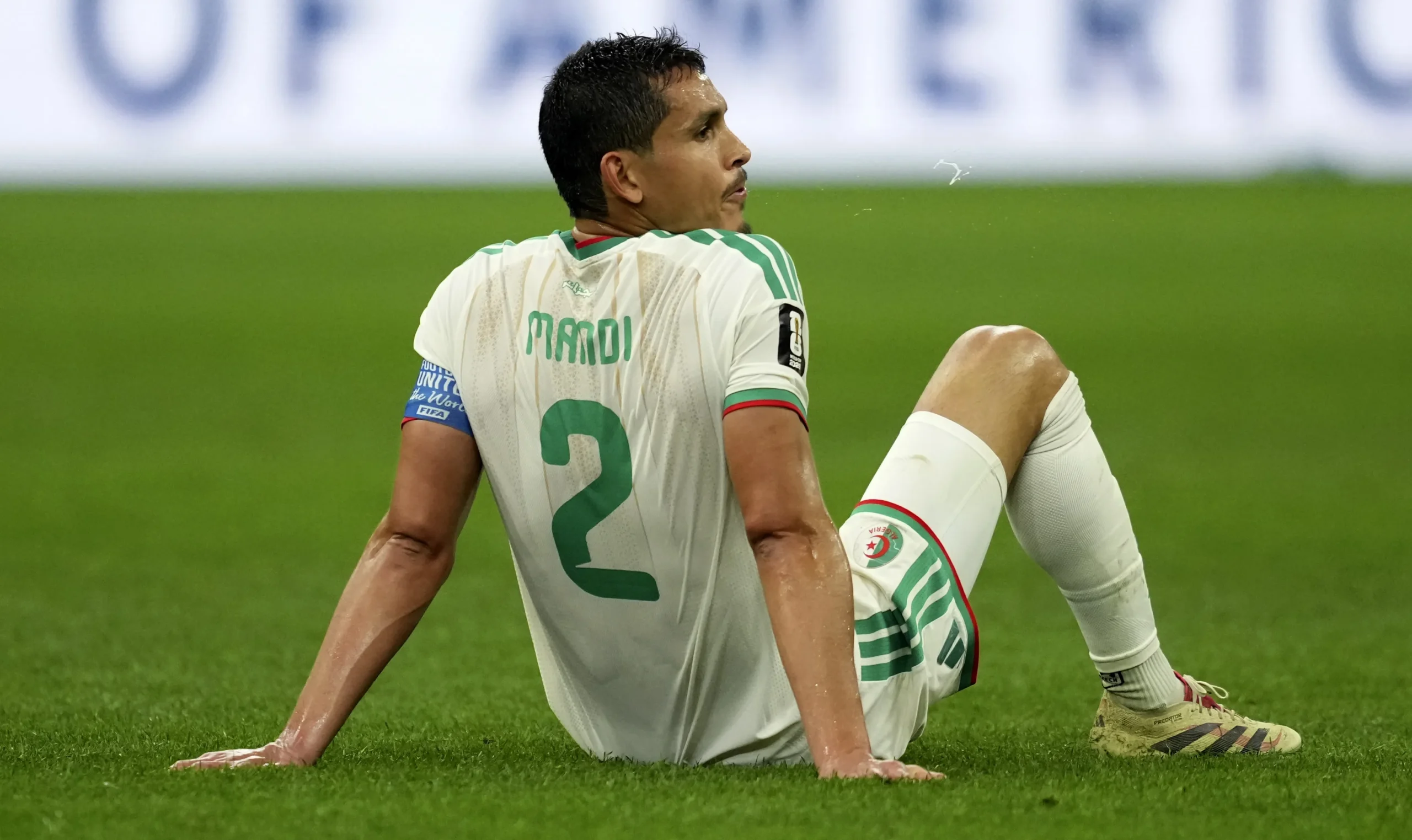 Soccer player kneels on a grass field, wearing a white and green jersey with the number 2 on his back, looking to the left. Soccer player kneels on a grass field, wearing a white and green jersey with the number 2 on his back, looking to the left.