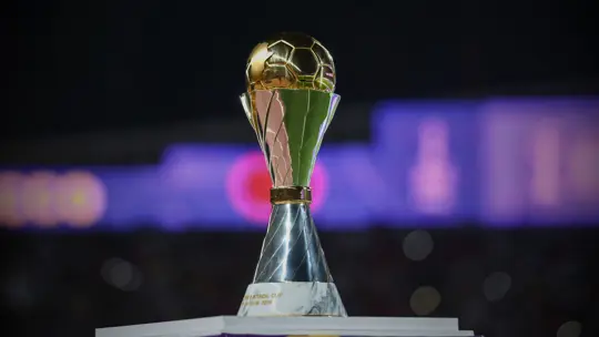 Gold trophy with a twisted blue stem on a white podium against a dark blurred background. Gold trophy with a twisted blue stem on a white podium against a dark blurred background.