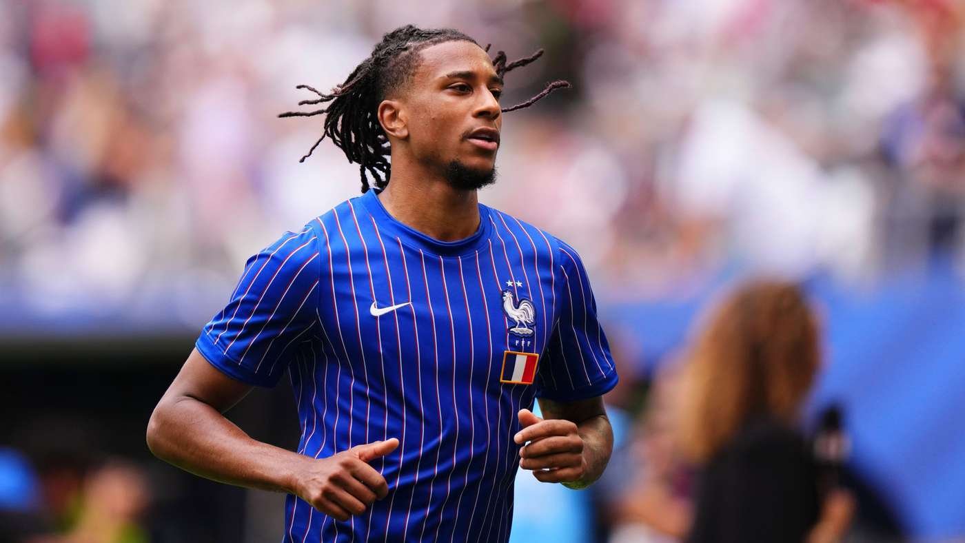 Soccer player in a blue France national team jersey runs on the field during a match with a blurred crowd in the background.