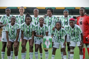 Women's soccer team in green-and-white striped jerseys posing for a group photo on the field, holding a banner with a circular crest. Women's soccer team in green-and-white striped jerseys posing for a group photo on the field, holding a banner with a circular crest.