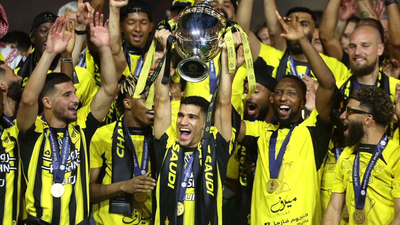 Celebrating team lifts trophy with ribbons; players in yellow and black jerseys wear medals nearby. Celebrating team lifts trophy with ribbons; players in yellow and black jerseys wear medals nearby.