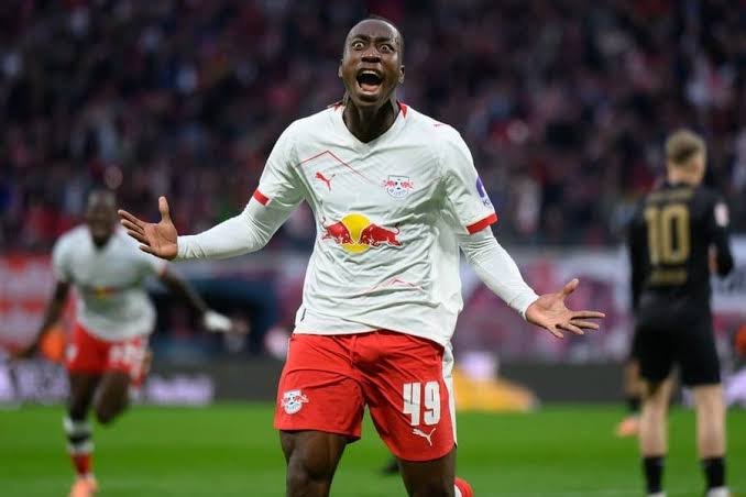 Soccer player in white jersey with Red Bull logo celebrating a goal with arms outstretched on the pitch.