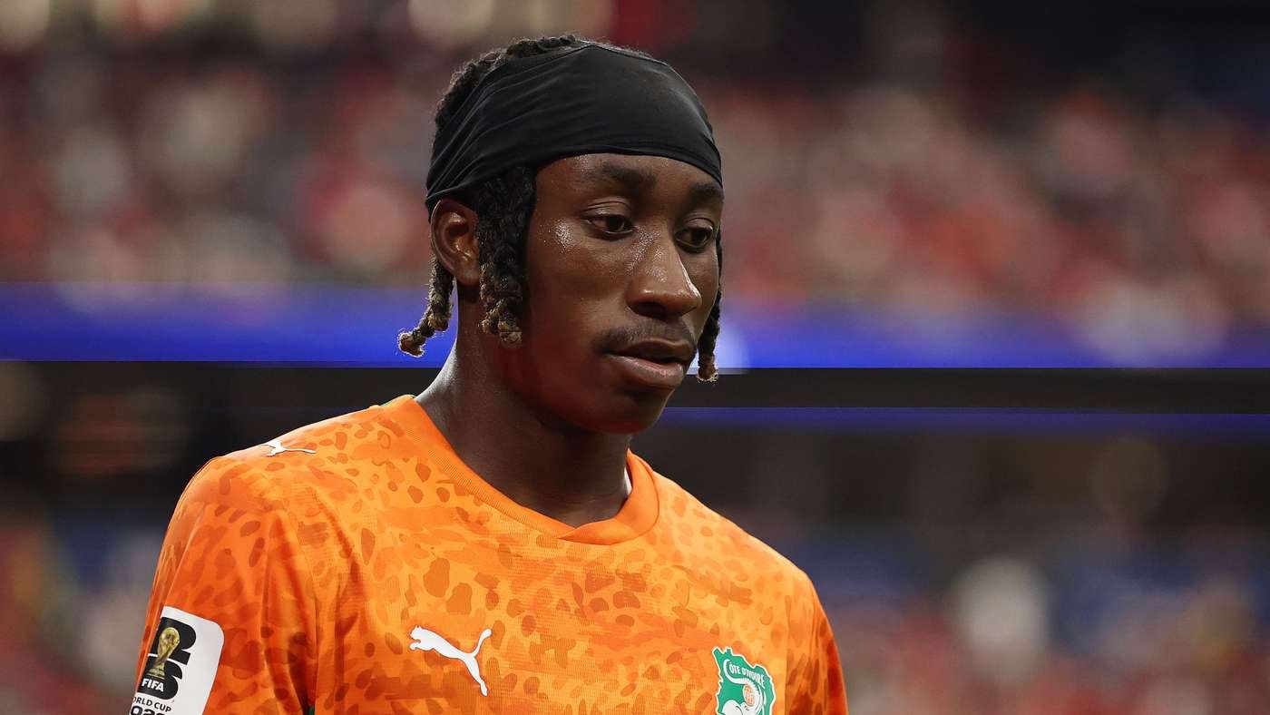 Close-up of a soccer player with a black headband and orange patterned jersey, looking down in concentration during a match.