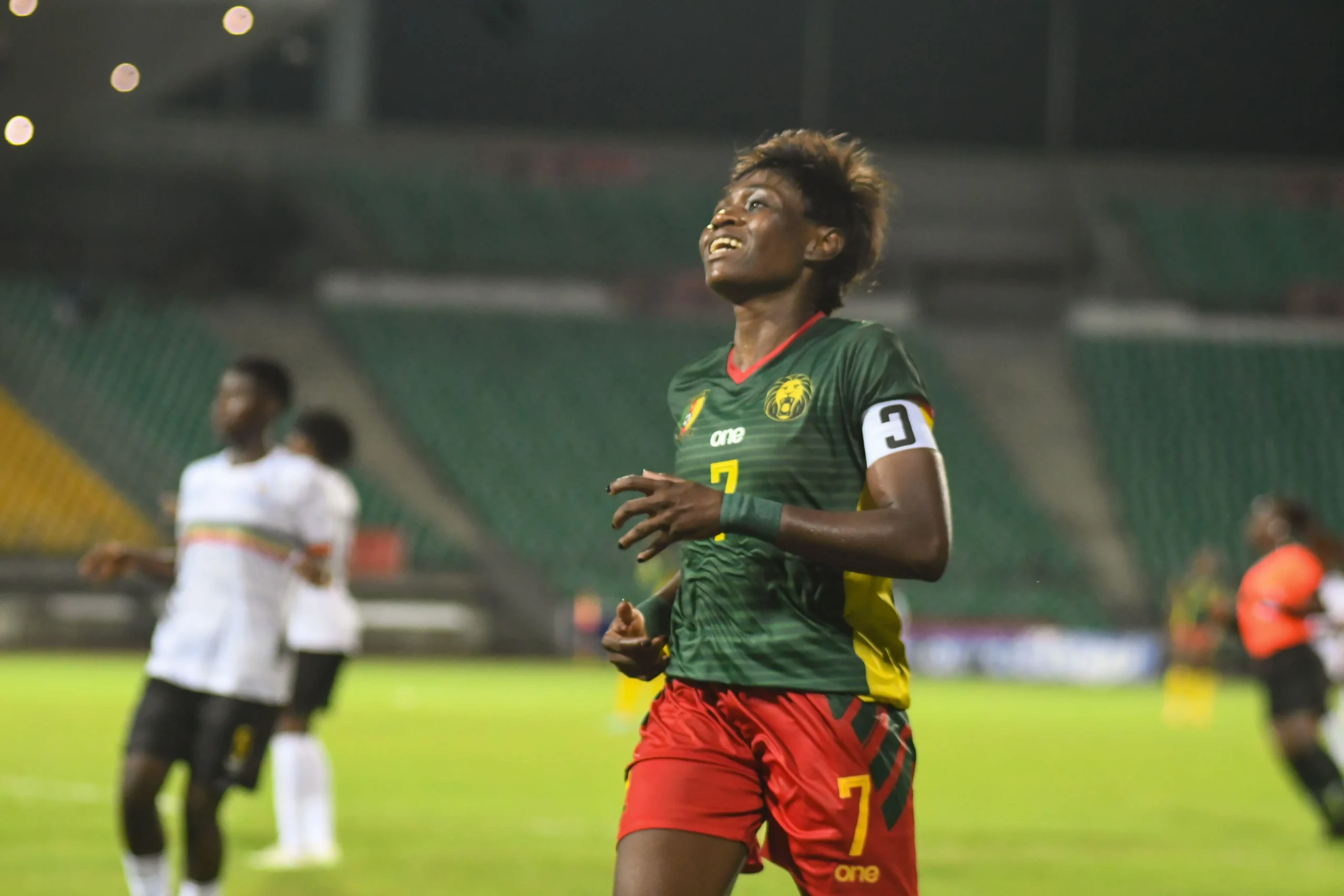 Soccer player in a green jersey with red trim and number 7, running on the field with a white captain's armband visible on his arm.