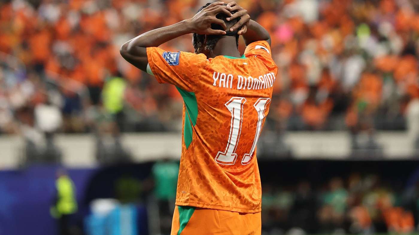 Soccer player in an orange kit, number 11, seen from behind with hands on head amid a cheering crowd.