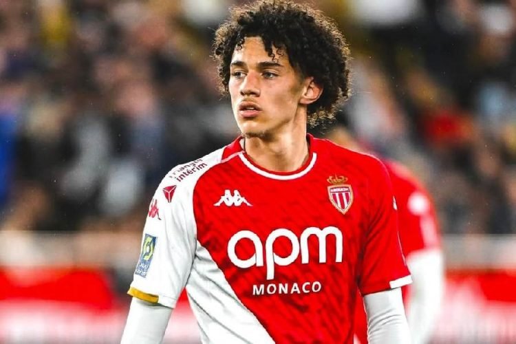 Soccer player in red-and-white Monaco jersey on the field, crowd blurred in the background, sponsor 'apm MONACO' visible on chest